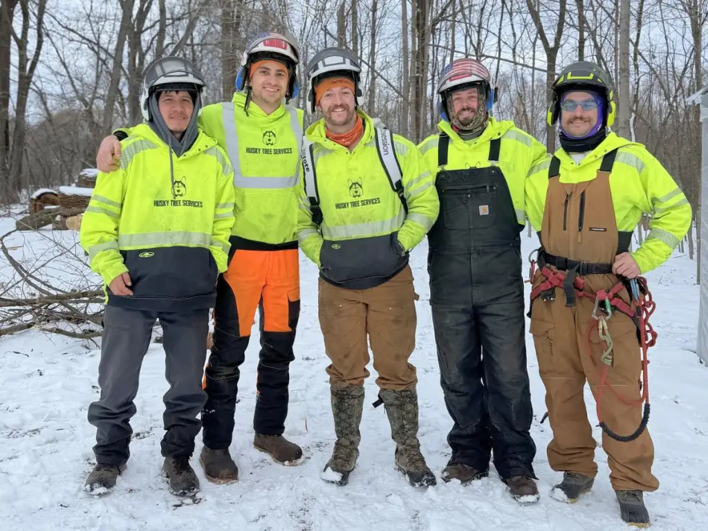 Five Husky Tree Services crew members in hi-vis jackets standing together in the snow